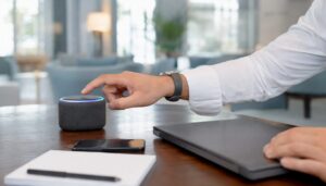 Eine Hand stellt ein smartes Assistenzgerät ein, das direkt neben einem Laptop mit dunklem Bildschirm steht.