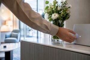 Eine Hand bedient ein leuchtendes KI-Gerät an der Hotelrezeption.