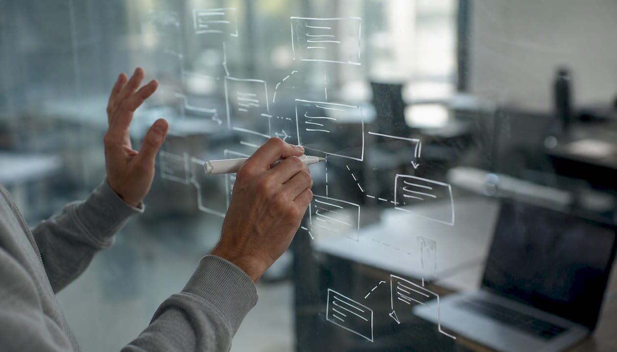 Hände, die ein Datenbankschema auf eine Glaswand zeichnen